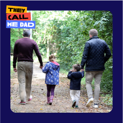 Two dads holding the hands of their two children while they are walking in a forest with their backs to camera and Movember lockup logo is above the image